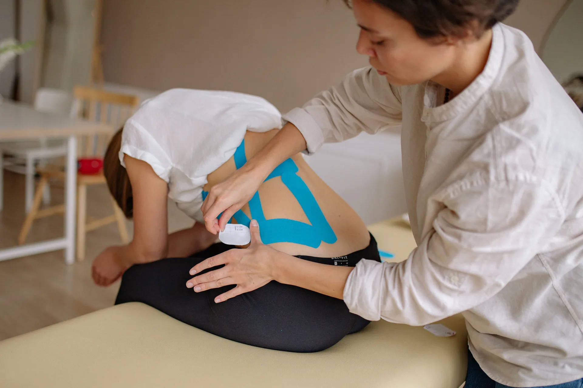 Rehabilitation practitioner applying kinesiology tape to a seated client